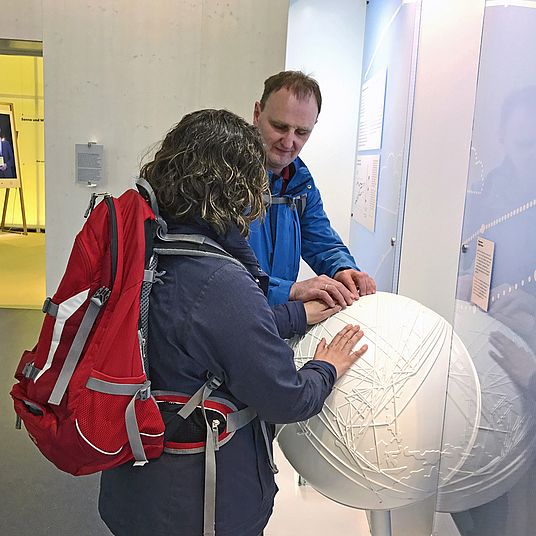 Besucherin und Besucher ertasten Weltkugel in der Sonderausstellung "energie.wenden".