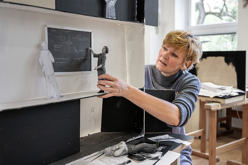 Bildhauerin Elisabeth Straßer hält die Figur, die vor einer Tafel steht. 