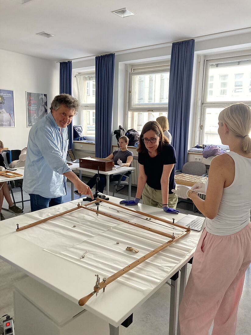 Der Personen stehen um einen Tisch mit verschiedenen Instrumenten, im Hintergrund weitere Personen