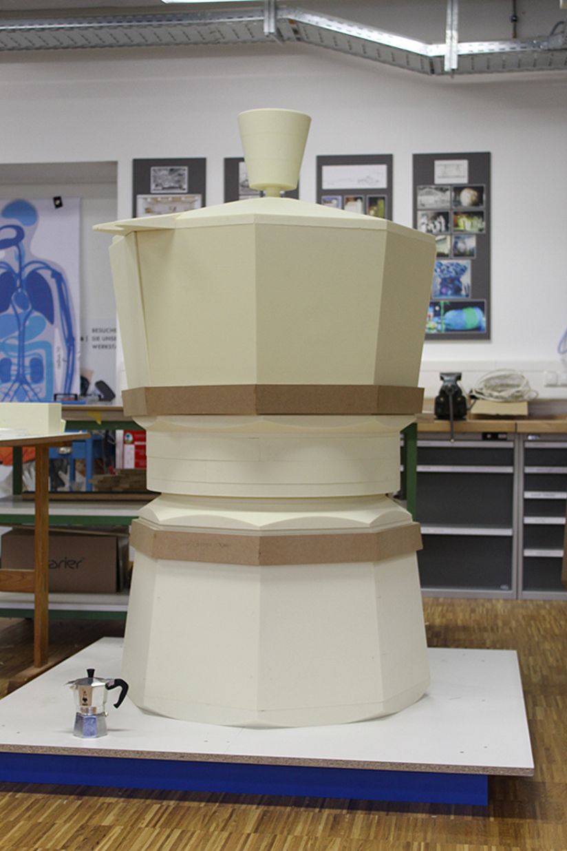 Nachbildung einer riesigen Espressomaschine. Daneben steht das kleine Original.