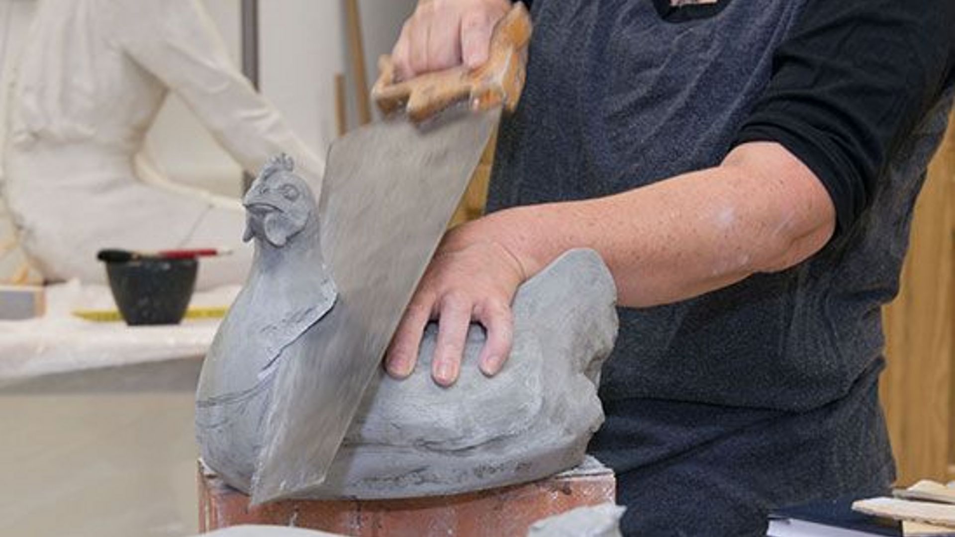 Bildhauerin schneidet geformten Huhn den Kopf ab.