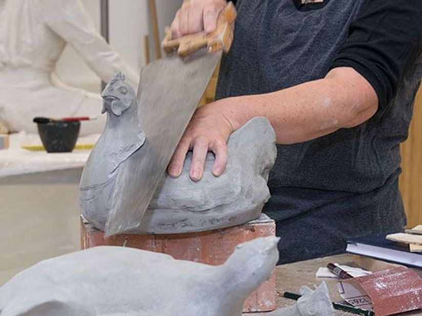 Bildhauerin schneidet geformten Huhn den Kopf ab.