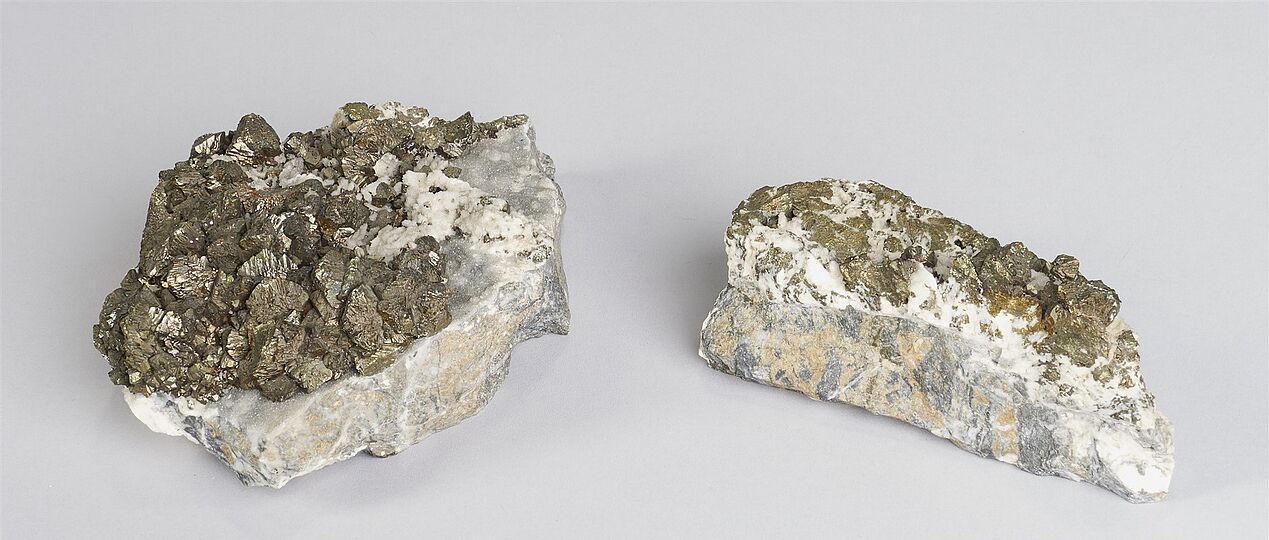 Zwei Erzproben von Chalkopyrit, einem Kupfererzmineral. Die goldgelben, metallisch glänzenden Kristalle sitzen auf heller und grauer Gesteinsmatrix.