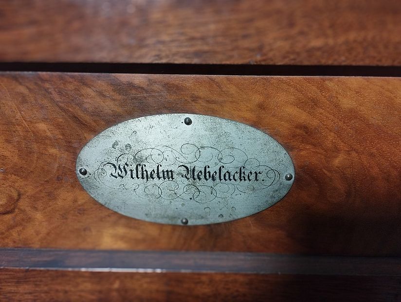 Detail zeigt eine Plakette mit schwungvoll geschriebenem Schriftzug "Wilhelm Uebelacker".