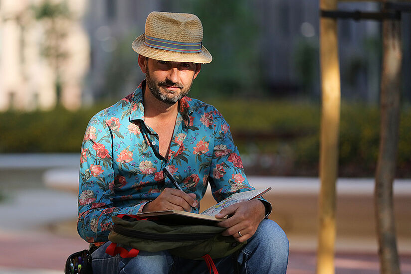 Lapin sitzt auf der Straße und zeichnet in seinem Skizzenbuch.