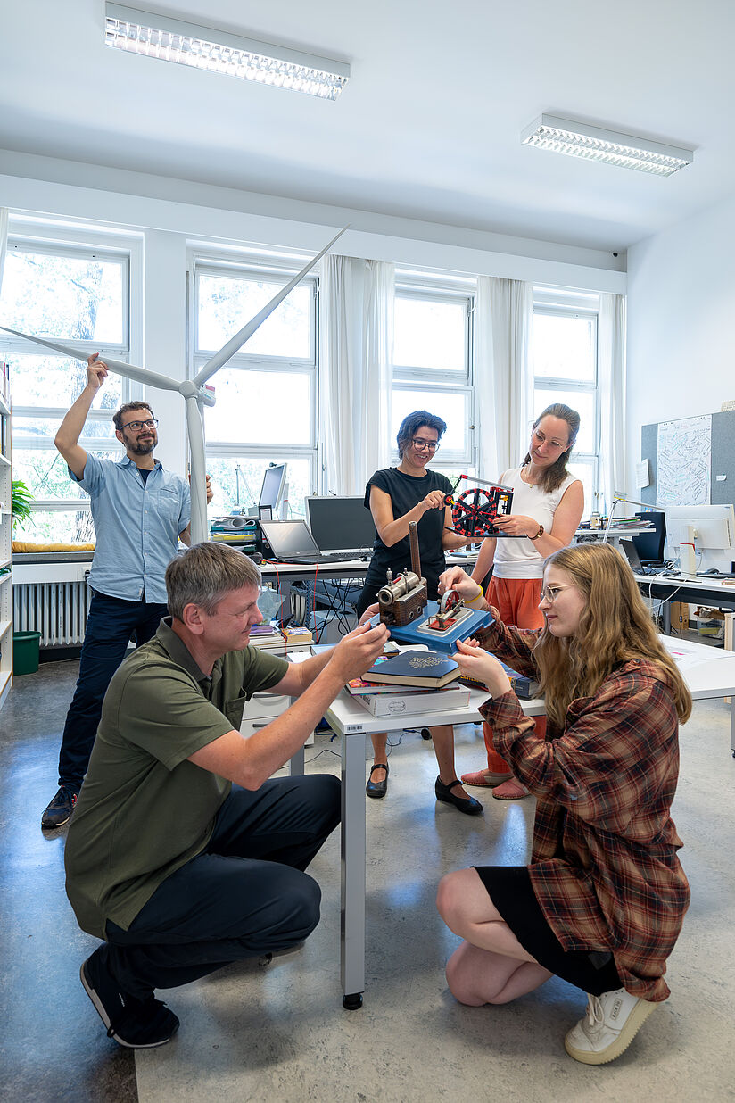 In einem Büroraum beschäftigt sich ein Team von fünfköpfiges Team von Kuratoren und Kuratorinnen mit technischen Modellen.