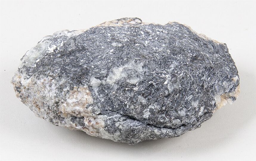 Erzprobe von Galenit. Dunkelgraues, metallisch glänzendes Mineral mit kristalliner Struktur in heller Gesteinsmatrix.