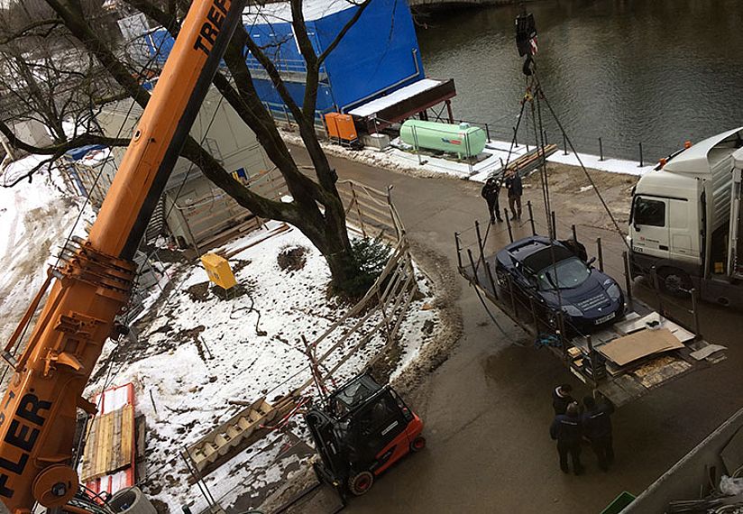 Ein Tesla wird mit Hilfe eines Krans in den Ausstellungsraum gebracht.