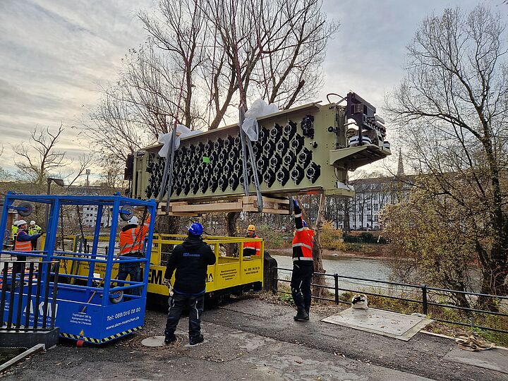 Das Mittelteil des Gezeitenrechners wird mit einem Kran, unterstützt von Menschenkraft, auf die Transportplattform gehoben,