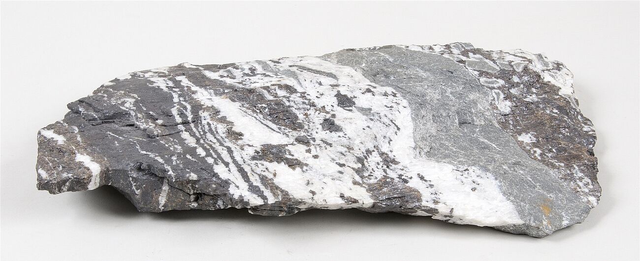 Erzprobe von Sphalerit. Dunkelgraues Gestein mit weißen, unregelmäßigen Adern und metallisch glänzenden Einschlüssen.