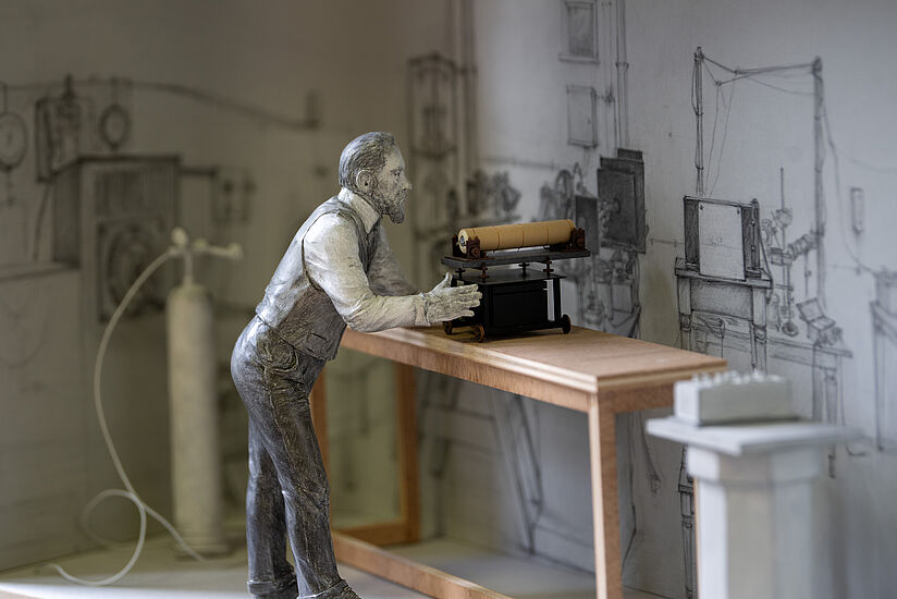 Eine Figur steht an einem Tisch vor einem wissenschaftlichen Instrument und führt Messungen durch.