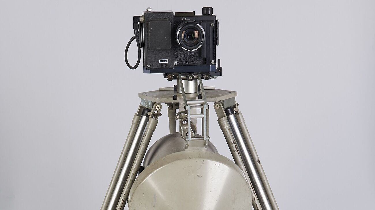 Fotografie einer Radaranlage: Graues Dreibeinstativ, Kamera oben montiert, darunter graue halbrunde Metallfläche (Radarsonde).