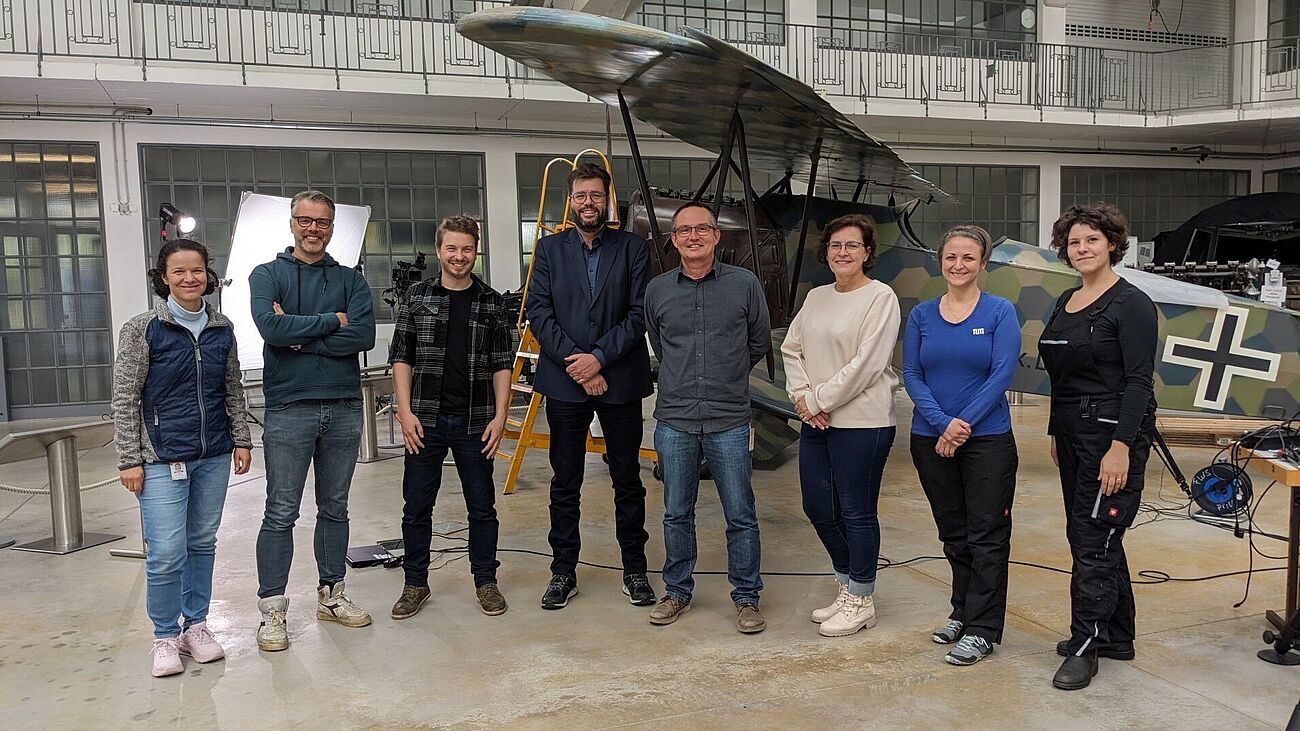 Foto: Provenienzforschung als internationale und interdisziplinäre Teamarbeit: Deutsche und niederländische Kolleg/innen vor der Fokker D.VII in der Flugwerft Schleißheim. (Von links: Marisa Pamplona, Konservierungswissenschaftlerin am Deutschen Museum, Jeroen Jazet, Dokumentarfilmteam NL, Andreas Hempfer, Kurator Deutsches Museum, Alfred Staarman, Kurator am Militärmuseum Soesterberg, Bernhard Wörrle, Provenienzforschung Deutsches Museum, Carla Marcus, Presseteam NL, Clarimma Sessa und Eva Mariasole Angelin, TUM School of Engineering and Design).