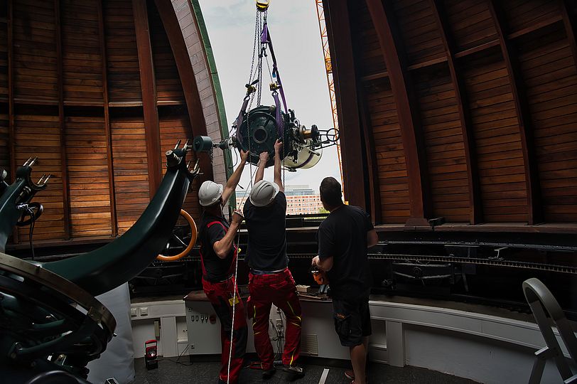 Museumsmitarbeiter richten das Teleskop zentimetergenau aus, damit es durch den Spaltschieber der Oststernwarte nach draußen gehoben werden kann.