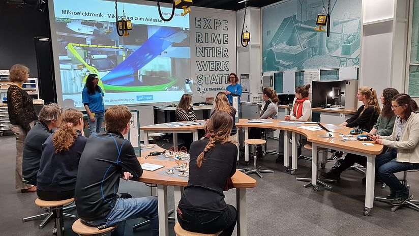 Menschen sitzen an einem U-Förmigen Tisch und folgen einer Präsentation. 