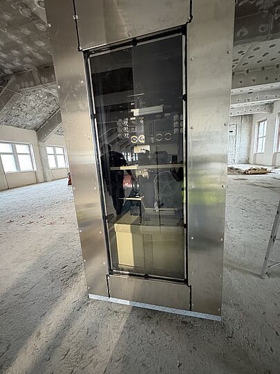 Blick auf die Schmalseite mit Fenster, durch das das Innere der Einhausung und der Rechner sichtbar sind.