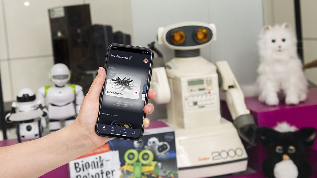 Hand hält Smartphone mit Deutsches Museum App in der Ausstellung Robotik
