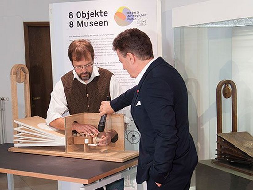 Alexander Steinbeißer, lässt den Nachbau "sprechen". Generaldirektor Heckl hält ein Mikrofon an den Sprechapparat..