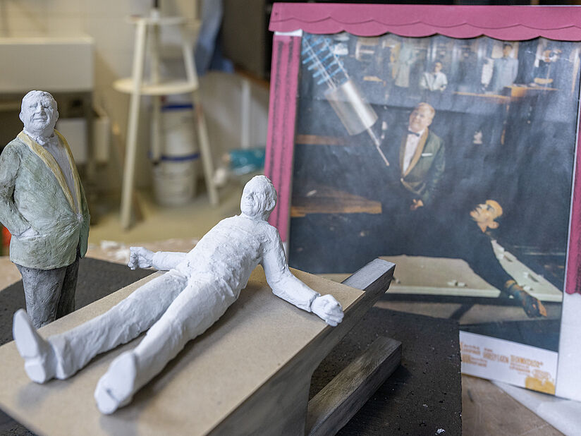 Ein Foto aus dem James Bond Film "Goldfinger" und davor die nachgebauten Filmhelden. Figuren 