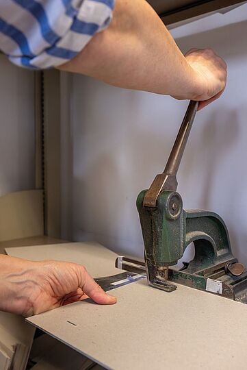 Photograph of the operation of a tool in a bookbindery. Apparently a cardboard is punched by the application of the tool.