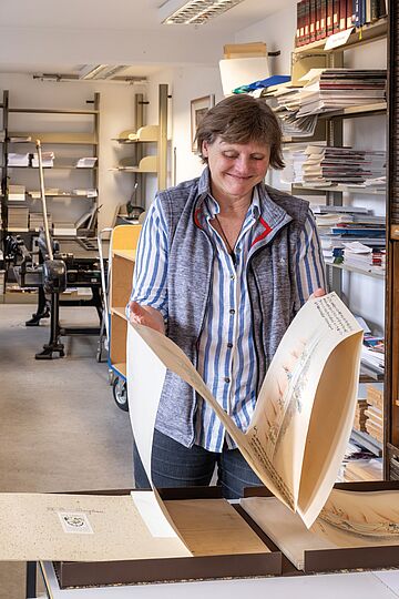 Fotografie einer Frau bei der Begutachtung eines ca. DinA-3-großen Papierbogens.