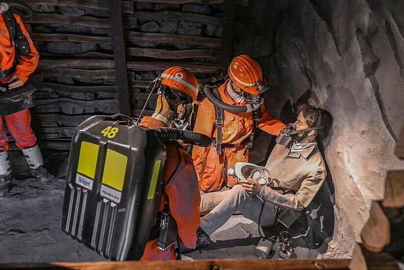 The scene depicts mine rescue workers treating an injured miner.