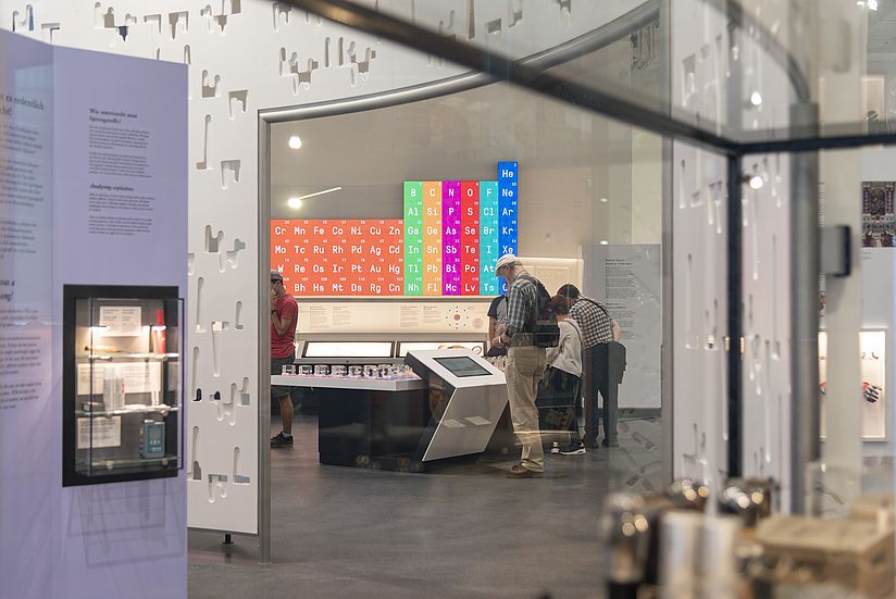 Blick in die Ausstellung Chemie An der Wand das Periodensystem der Elemente, davor Besuchende an der Medienstation zum Periodensystem.
